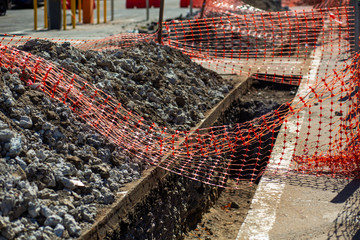 Repair work on the city street. A freshly dug trench is fenced with a net, for the safety of citizens.