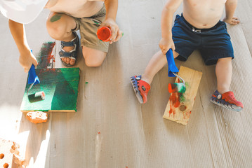 two boys in shorts are sitting on the floor and playing with paints