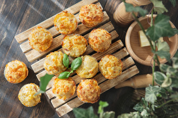 Homemade savory muffins with cheese, herbs on a wooden plate, dark background with green plants. Fresh baked,  healthy snack or breakfast meal. Natural light. 