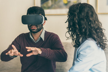 Front view of tranquil young man testing virtual reality headset. Hispanic man experiencing VR...