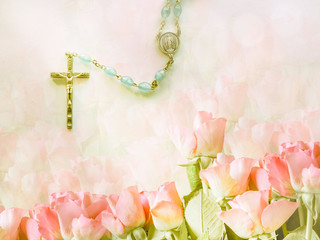 Rosary on a rosy background, group of red roses fading on a background, a beam of light illuminating the rosary, religious background with copy space