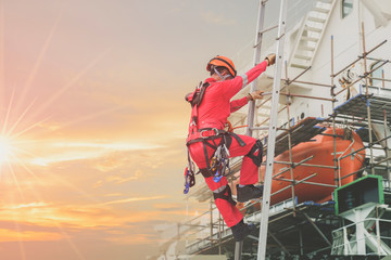 Worker on fixed ladder, Rope access Safety concept in shipyard worker wearing equipment protective full safety harness, at high places on side ship cargo ship during ship maintenance in shipyard.