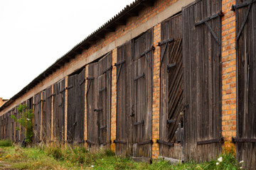 Old cowshed. Large wooden gate and dried wood. Old brick building