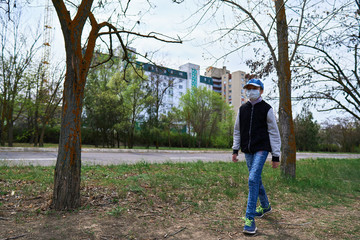 child girl walks down the street during the day, a pedestrian walkway and high-rise buildings with apartments, a residential area, a medical mask on her face protects against viruses and dust