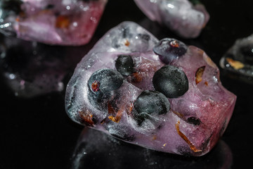 Black currant berries frozen in ice with reflection on dark background. Cracked ice. Closeup, selective focus