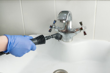 cleaning  white bathroom sink and tap with steam generator, hand in blue glove holds black hose with brush, which produces steam, home cleaning concept, mold and calcium control