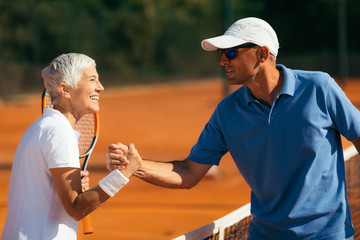 Tennis Instructor with Senior Woman in her 60s Handshaking after Having a Tennis Lesson on Clay Court.