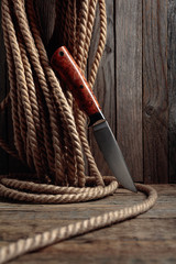 Hunter combat hand made knife and hemp rope on wooden background.