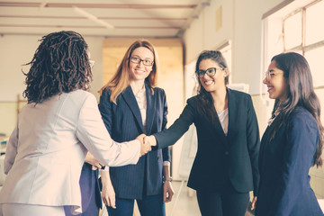 Smiling young businesswomen shaking hands in office. Confident cheerful business partners greeting each other. Business concept