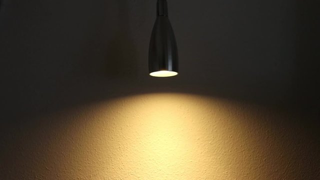 A dimmable light in a dark room and its effect on a wall. The brightness of the light increases and decreases. The dimmer is set on a small led light
