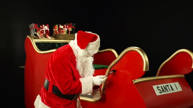 Santa Claus painting his sleigh with a paintbrush. Father Christmas preparing for the big day on a black background. Stock Video Clip Footage