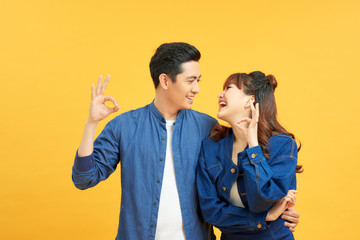 Young beautiful couple standing over isolated yellow background doing ok gesture with hand smiling, with happy face.