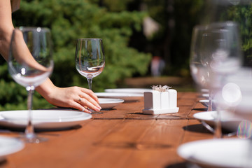 Girl the waiter in a summer cafe under the open sky arranges the dishes on a wooden banquet table.