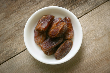 Selective focus adn top view of a dried dates fruit in a white bowl on wooden background. Ramadan holy month for muslim concept where they are fasting.