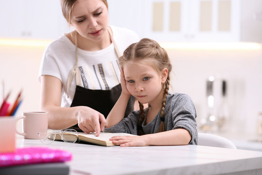 Woman helping her daughter with homework at table in kitchen