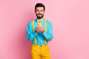 Portrait of his he nice attractive cheerful cheery bearded brunette guy holding in hands cell chatting online internet browsing isolated over pastel pink color background