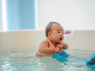 Fototapeta na wymiar 3 months little Asian baby girl learning to swim in an indoor pool.