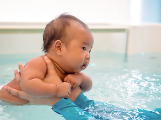 Fototapeta na wymiar 3 months little Asian baby girl learning to swim in an indoor pool.