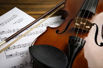 Beautiful violin, bow and note sheets on wooden table, closeup