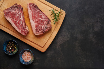 Raw Dry Aged Beef Steak. Raw Dry Aged Meat. Raw sirloin steak on a wooden board with four peppers blend, himalayan salt, and rosemary. black slate stone background