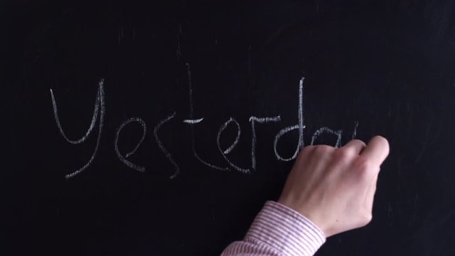 Yesterday with chalk on a blackboard. Top view of the yesterday written in chalk on the board. Yesterday, in a shirt, the hand writes in english