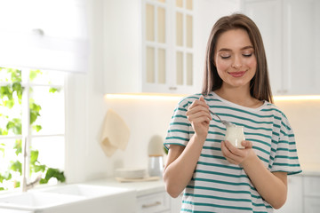 Young attractive woman with tasty yogurt in kitchen. Space for text