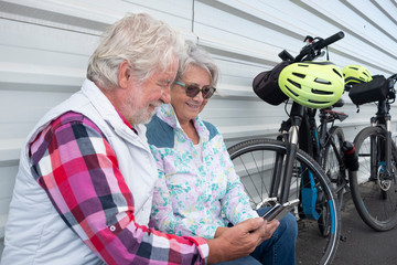 A couple of senior people stop riding with their electric bicycle to look the mobile phone together.  Smiling attractive elderly persons , casual clothing