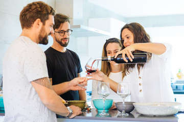 Beautiful young woman pouring wine in glasses. Group of cheerful people standing near table. Wine tasting concept