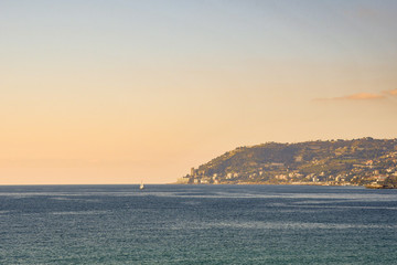 Fototapeta premium Mediterranean seascape with a cape and a sailboat on the sea horizon at sunset, Sanremo, Capo Nero, Imperia, Liguria, Italy