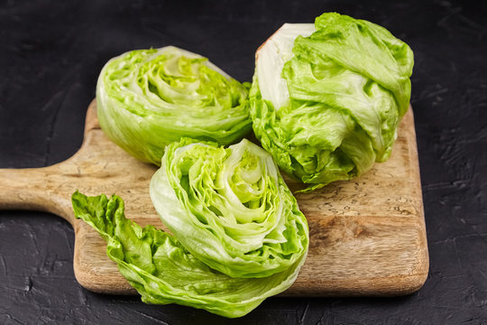 Iceberg lettuce on wooden cutting board on black stone table background. Two halves and one whole crisphead lettuce