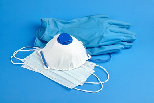 Respirator, Medical Sanitary Surgical Masks And Rubber Gloves On Blue Background. Face Masks Provide Protection Against The Spread Of Infection