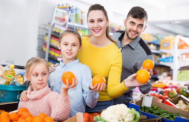Happy family with two little girls looking for fresh oranges in supermarket