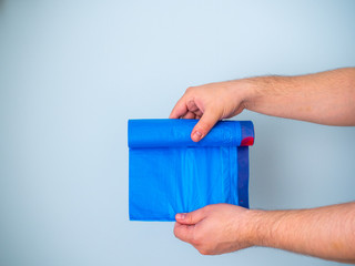 Men's hands holding a new blue plastic garbage bag isolated on a blue background
