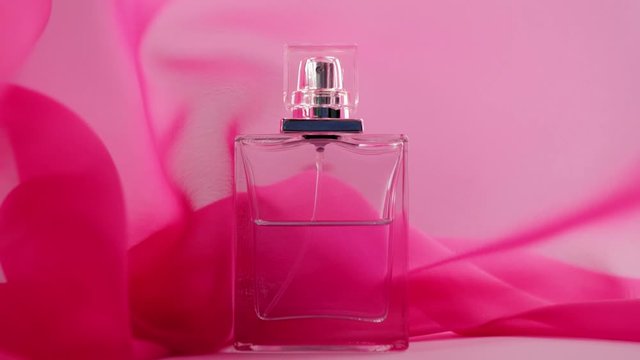 Flat surfaced perfume bottle with cyan perfumes or essential oils is on the table. Pink fabric flutters around and waves in the air around the perfume bottle. Concept of aroma and smell. Close up