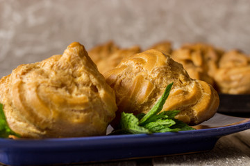 Delicious big cream puffs with cream in hand painted blue oval saucer with mint leaves on aged wooden background. Selective focus.