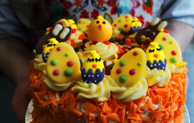 Fototapeta na wymiar bright yellow and orange Easter cake with lots of sweets for decoration, two hands holding the cake
