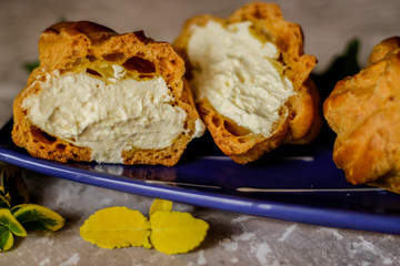 Delicious big cream puffs with cream in hand painted blue oval saucer with mint leaves on aged wooden background. Selective focus.