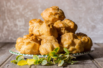 Delicious big cream puffs with cream on aged wooden background. Selective focus.