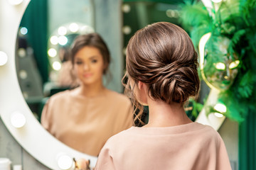 Beautiful young woman with hairstyle looking in the mirror at beauty salon.