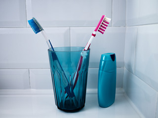 A BLUE GLASS WITH TWO TOOTHBRUSHES, ONE PINK AND ONE BLUE