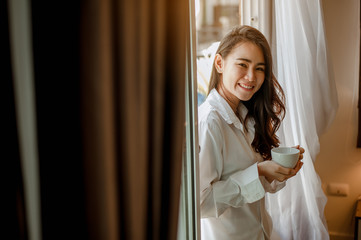 Young woman asia living at home relaxing and drinking cup of hot coffee in the bedroom on holiday. Asian, asia, relax, alone, technology, lifestyle concept.