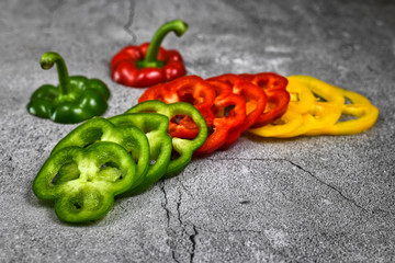 Cut slices of yellow, red and green bell pepper vegetables in a row on gray background