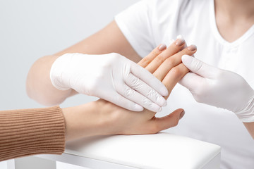 Manicurist is holding fingers of woman with beige manicure in salon.