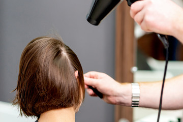 Fototapeta premium Back view hairdresser's hand drying hair of woman by hair dryer in hair salon.