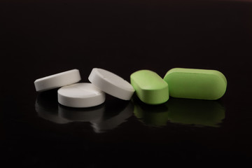 White and green pills are on a black reflective table. Medical pills.