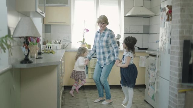 Grandmother Dances In The Kitchen With Two Little Granddaughters.
