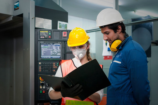 Industrial engineer worker woman and man wearing helmet, holding and looking at black file folder of document, discussing and working together at manufacturing plant factory, young people working in i