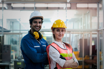 Portrait of industrial engineer worker woman and man wearing helmet standing with arms crossed at manufacturing plant, young people working together at manufacturing plant industry factory