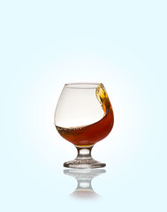 Glass glass with an alcoholic drink or cognac and splashes on a light background. Isolated, splash.