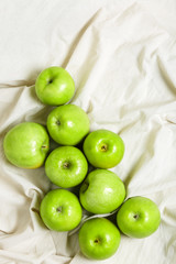 Green apples on a light fabric background. Harvest apples, summer season, fresh fruits. Top view, flat lay.
